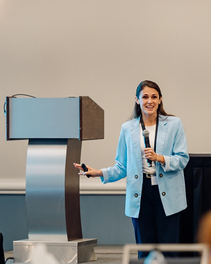 Dr. Johnston holds a microphone next to a podium and smiles and gestures in a presentation,