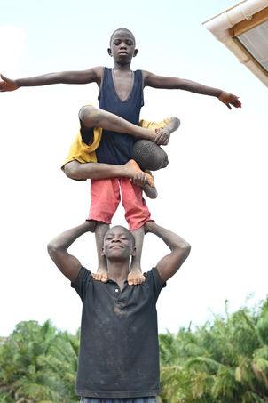 A boy stands on his brother's shoulders while his other brother is wrapped around him