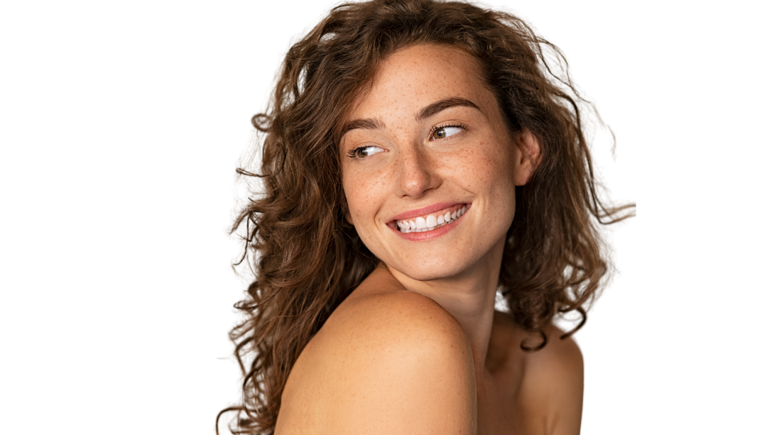Smiling woman looks back, with curly hair and bare shoulders in studio.