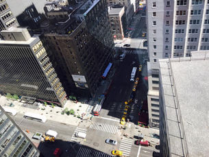 Blick von oben in eine enge Straßenschlucht einer Großstadt. Hohe Gebäude werfen lange Schatten auf eine Kreuzung mit Autos und Menschen. Perspektive von oben als Metapher für Komplexität und das „Rabbit Hole“ unserer modernen Informationswelt.