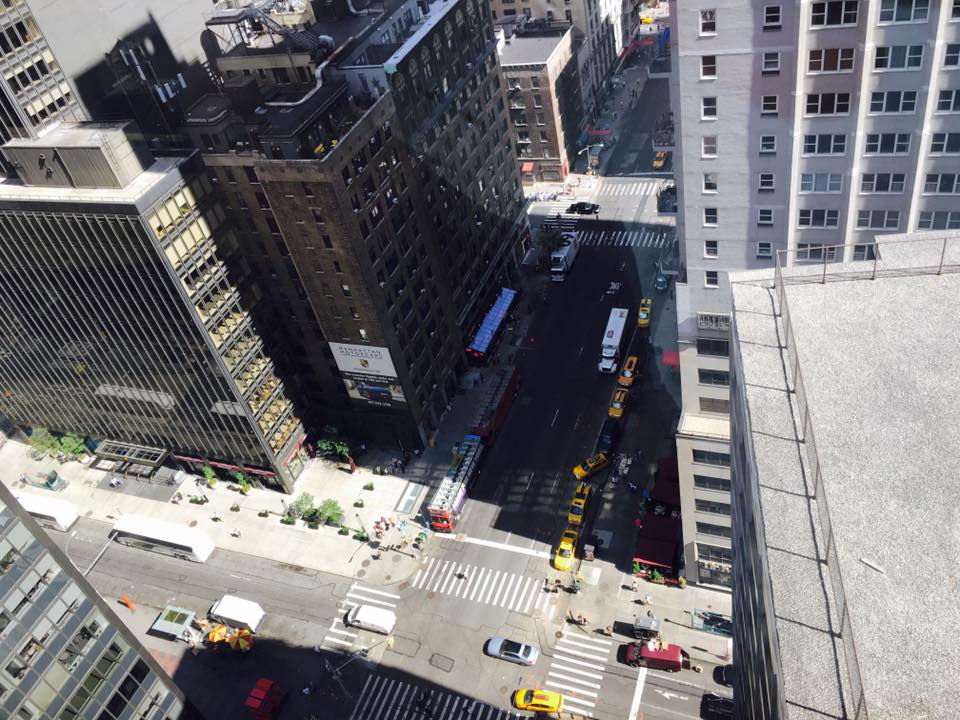 Blick von oben in eine enge Straßenschlucht einer Großstadt. Hohe Gebäude werfen lange Schatten auf eine Kreuzung mit Autos und Menschen. Perspektive von oben als Metapher für Komplexität und das „Rabbit Hole“ unserer modernen Informationswelt.