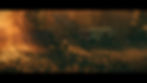 Man walks in orange-lit trailer park surrounded by trees and old vehicles, creating a serene, moody atmosphere at sunset.
