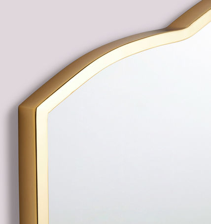Corner of aged brass frame mirror with scalloped shade on top