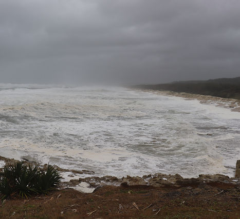 Main Beach, Minjerribah/ North Stradbroke Island just before Cyclone Alfred hit. The ocean is all white wash and foam. Most of the beach is washed away forming a steep drop off. Thick grey clouds and rain in the distance 