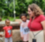 a teacher with two of her students outside in the field smiling and teaching them something.