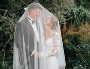 Bride and groom laughing together under veil in gardens of Michelham Priory wedding venue