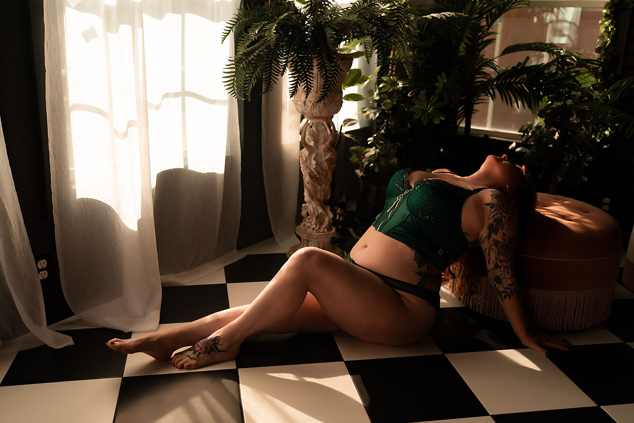 Nature-inspired boudoir image of a client in emerald green lingerie, posed amid lush greenery in the Greenhouse Set at BoudoirXAllie