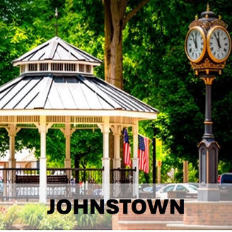 A white gazebo with an American flag next to a historic clock tower in a Johnstown Ohio public park.