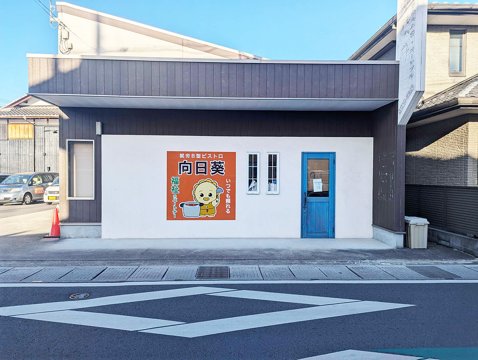 就労継続支援B型ビストロ「向日葵」の外観。白い壁に青い扉、看板にはキャラクターと「いつでも頼れる福祉のパートナー」の文字が描かれている。