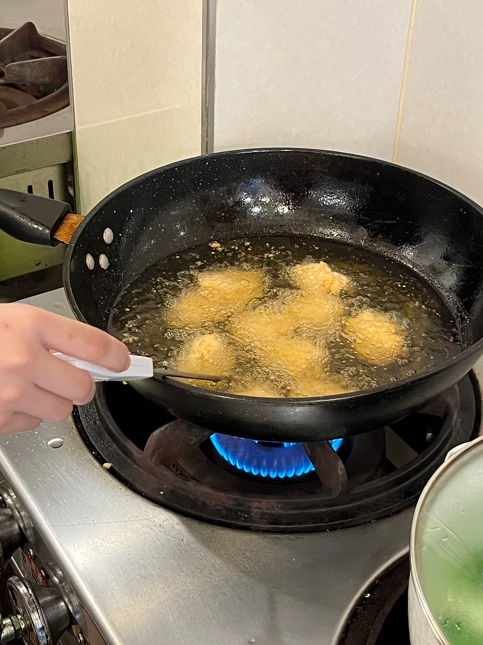 ジュージューという音と揚げ物の香りが伝わってくる、家庭のキッチンでの調理風景。フライパンの熱い油で、手作りの唐揚げかチキンナゲットが黄金色に揚がっています。