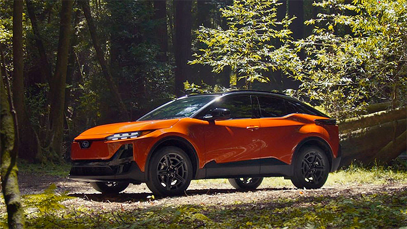 ubaru Uncharted 2026 color naranja estacionada en un entorno natural boscoso, SUV compacto de diseño moderno y aerodinámico, similar al Toyota C-HR+, ideal para aventuras y conducción todoterreno