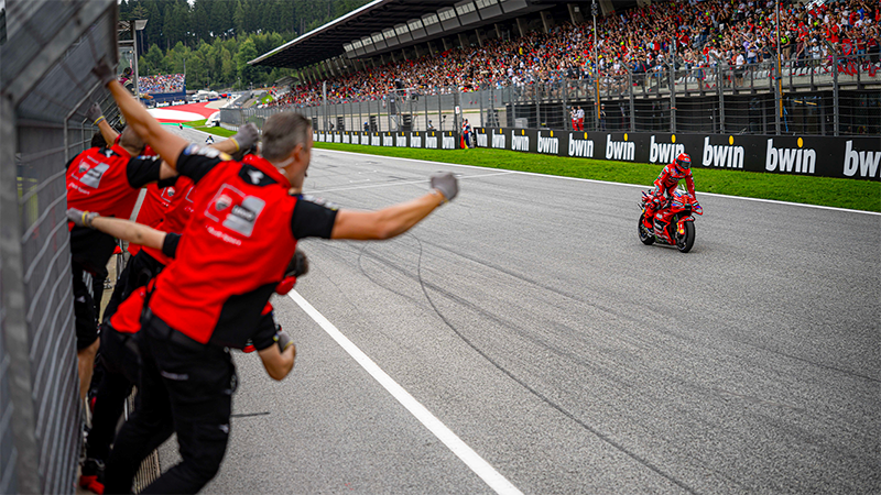 Marc Márquez cruzando la meta en primer lugar frente a su equipo en el Gran premio de Austria de MotoGP 2025