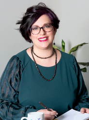 Founder of SWAN - Strong Women Arise Network wearing dark green, with a pen in her hand and a notebook, with a coffee mug on the table.