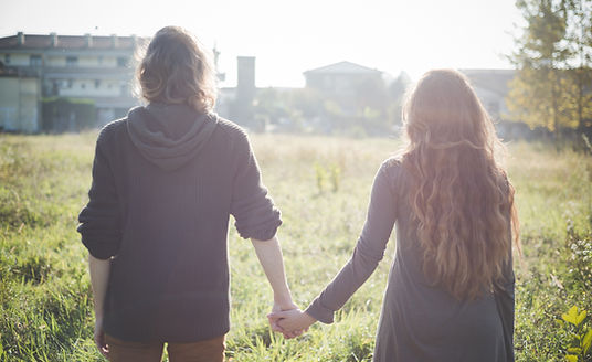 Two people holding hands, walking through a field, symbolising support and connection in relationships.