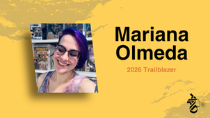 Smiling person with purple hair, glasses, and a colorful shirt. Background has shelves of comics. Text reads "Mariana Olmeda 2026 Trailblazer."