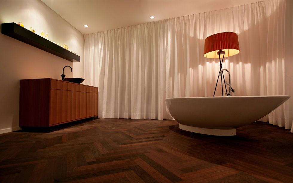 Spa-Raum mit dunklem Parkett, organischer Badewanne, Eichenmöbel mit Aufsatzwaschbecken und beleuchtetem Wandboard, dahinter raumhoher Vorhang