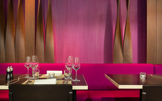 Gedeckter Tisch mit perlgoldener Kante vor magentafarbener Wand mit aufwändig gedrehten Holzlamellen