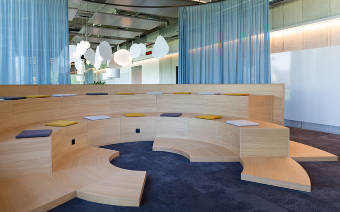 Auditoriumeinrichtung aus Holzstufen in kreisrunder abgestufter Anordnung mit Sitzkissenund raumhohem Vorhang als Raumteiler