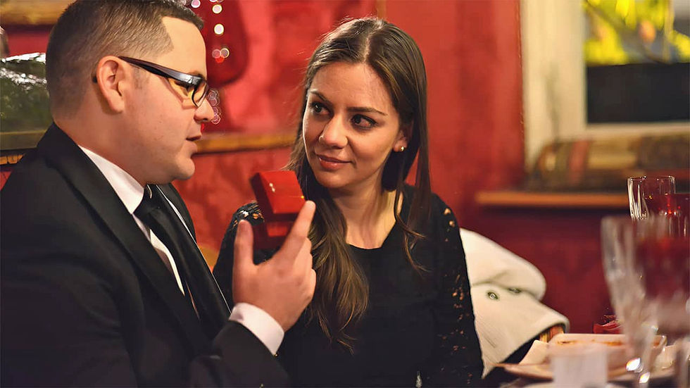Homme en costume cravate tenant un écrin rouge avec bague de fiançailles pour demander en mariage une femme brune