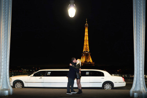 Couple s’embrassant devant une limousine blanche avec tour Eiffel scintillante de nuit