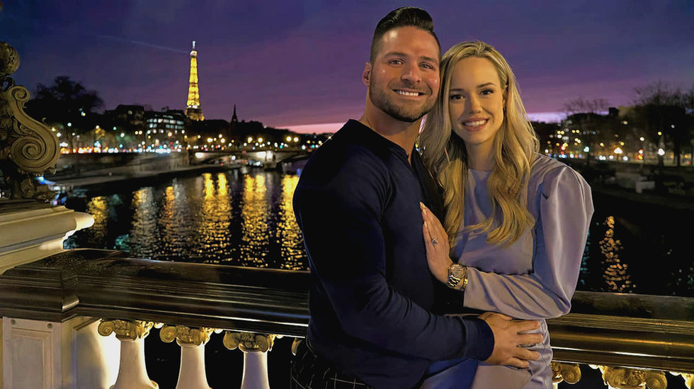 Homme et femme blonde posant sur un pont de Paris avec vue sur la Tour Eiffel. Coucher de soleil aux nuances violettes