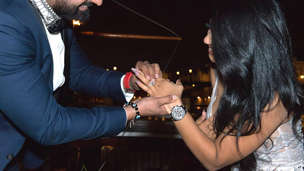 Brunette woman smiling as she looks at the engagement ring her fiancé is placing on her finger in Paris