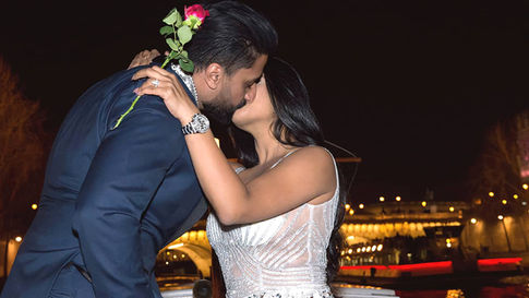Woman in a white dress holding a red rose and kissing a man in Paris at night