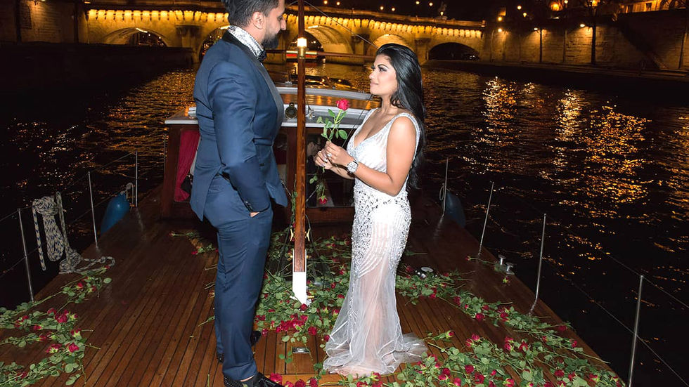 On a boat covered in red roses in Paris, a man in a suit and a woman in a dress looking at each other affectionately
