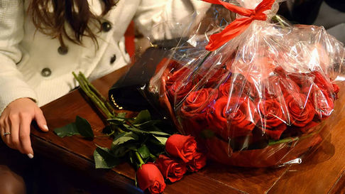 Sur une table de restaurant, bouquet de roses rouges contenant une boîte métallique rouge en forme de cœur