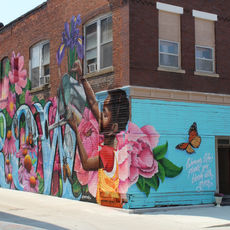 GROW by Mural Mafia (Menace, Resa, Lindsay, Canas) from 2021. The mural shows two children watering many flowers that surround the word "GROW".  Flowers include those native to Iowa including peonies, irises, wildroses, and coneflowers.
