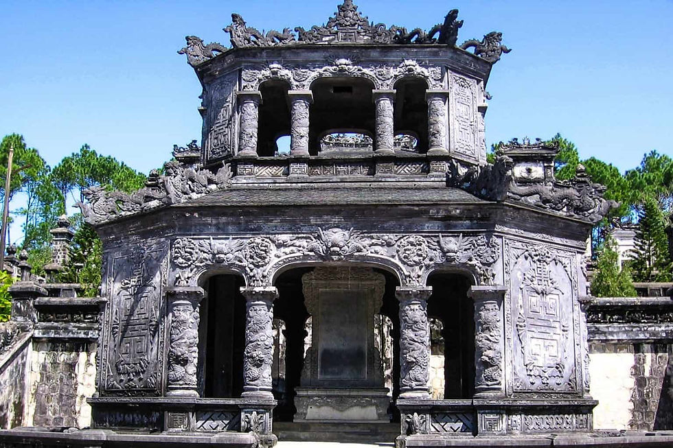 Image of an intricately carved, ancient stone structure with multiple tiers and a central entrance. The edifice features ornate decorations and statues, possibly from an Asian culture, set against a clear sky with lush vegetation in the background. The historical and architectural significance of the structure makes it interesting and relevant.