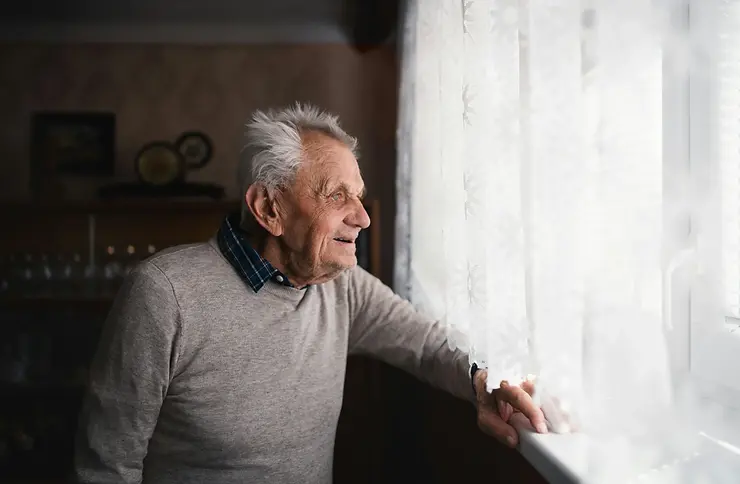 Elderly man reaching for utensils on pull-out shelves in a lowered kitchen cabinet, illustrating ADL services and homecare assistance for Fort Worth senior care.