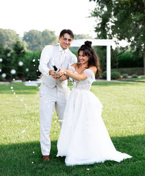 A bride and groom popping a bottle of champagne.