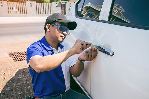 Young Man Opening White Car Door With Lockpicker. Professional making key in locksmith.jpg