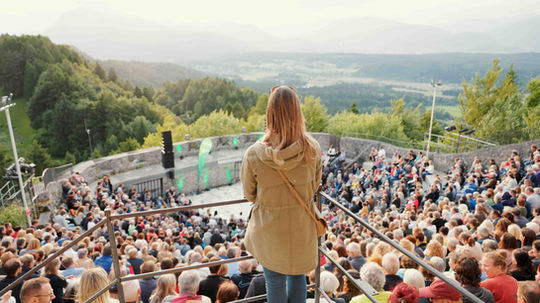 Eine Frau blickt von oben auf die gut besuchte Burgarena Finkenstein mit weitem Ausblick über das Tal.