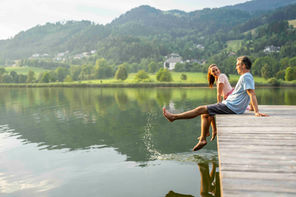 Paar sitzt entspannt auf einem Holzsteg am Urbansee und lässt die Füße im Wasser baumeln.