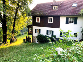 Seitenansicht eines Hauses am bewaldeten Hang im Abendlicht mit Blick Richtung Millstätter See