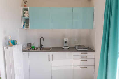 Helle Küchenzeile mit Spüle, Arbeitsplatte, Oberschränken in Mint und einer weißen Kaffeemaschine.