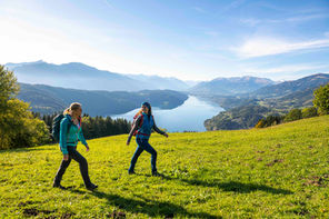 Zwei Frauen wandern auf einer grünen Almwiese mit weitem Panoramablick auf den Millstätter See.