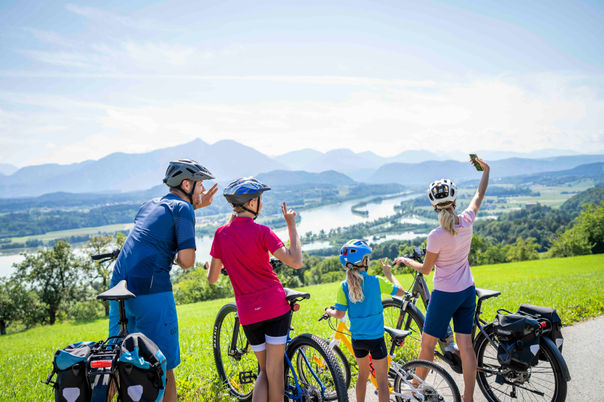 Eine Familie mit Fahrrädern macht ein fröhliches Selfie vor einer weiten Seenlandschaft in Kärnten.
