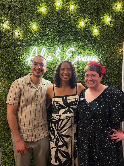 Three people smiling together outdoors with greenery, celebrating a joyful moment.