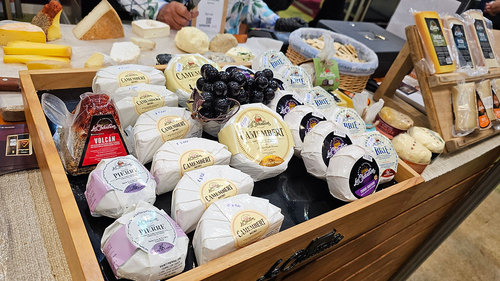 Plateau de fromages emballés (Camembert, Brie, Saint Pierre) avec raisin noir sur un étal de marché.