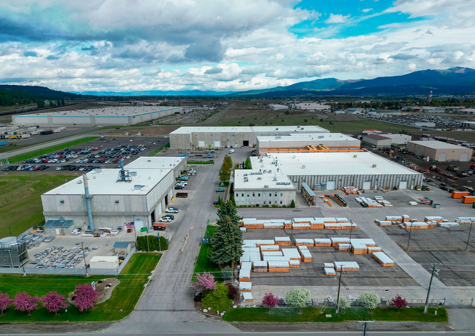 Aerial photo of Wagstaff, Inc. headquarters in Spokane Valley, Washington. Blue sky with clouds, green grass, cherry blossom trees in bloom with pink flowers. 