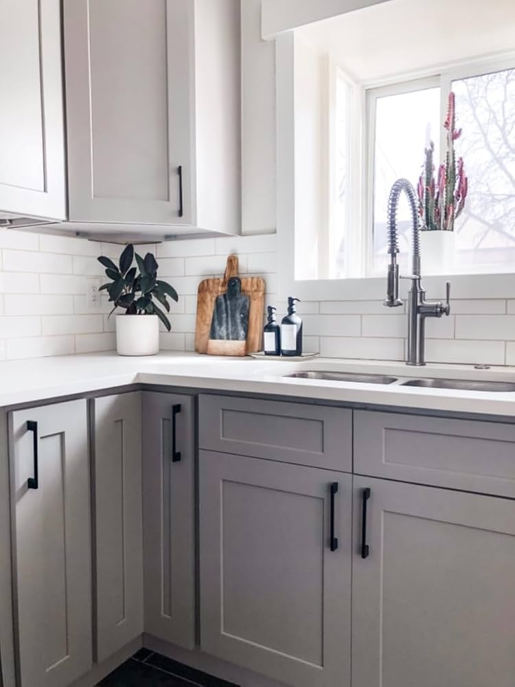 Modern kitchen with white cabinets, a stylish faucet, and a potted plant. Cutting board and soap bottles on the counter. Bright ambiance.