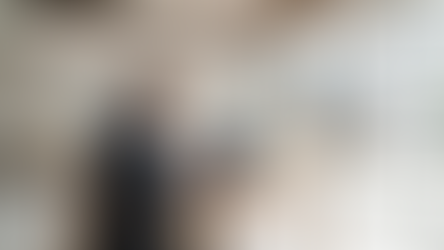 Man in suit works on laptop displaying statistics in a modern, partially constructed room with virtual room projection, featuring a sofa.