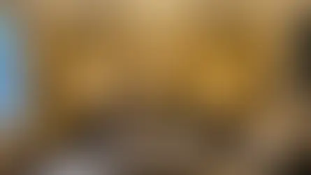 Elegant living room with a velvet sofa, ornate mirror, and chandeliers. Warm lighting enhances gold walls. Candlelit coffee table with flowers.