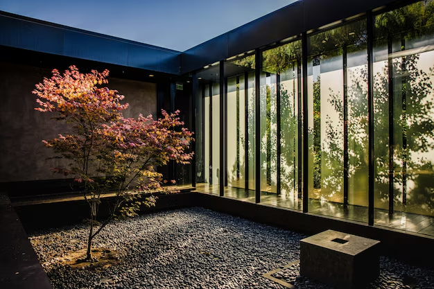 Sunlit courtyard with a tree shedding pink leaves, surrounded by glass walls reflecting shadows. Stone slab on gravel ground, serene atmosphere.
