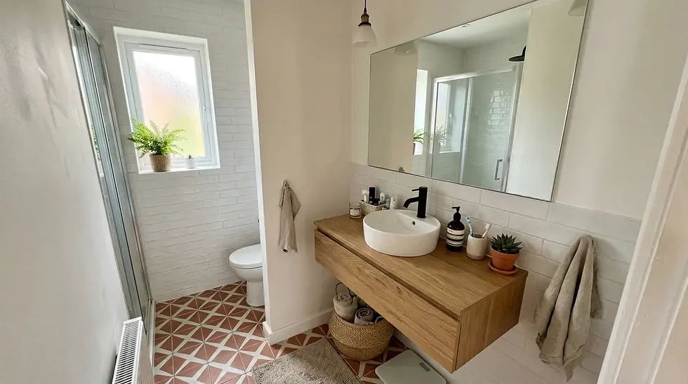 Modern bathroom with a wooden vanity, white sink, and black faucet. Potted plants by a window. Geometric tiles and a large mirror.