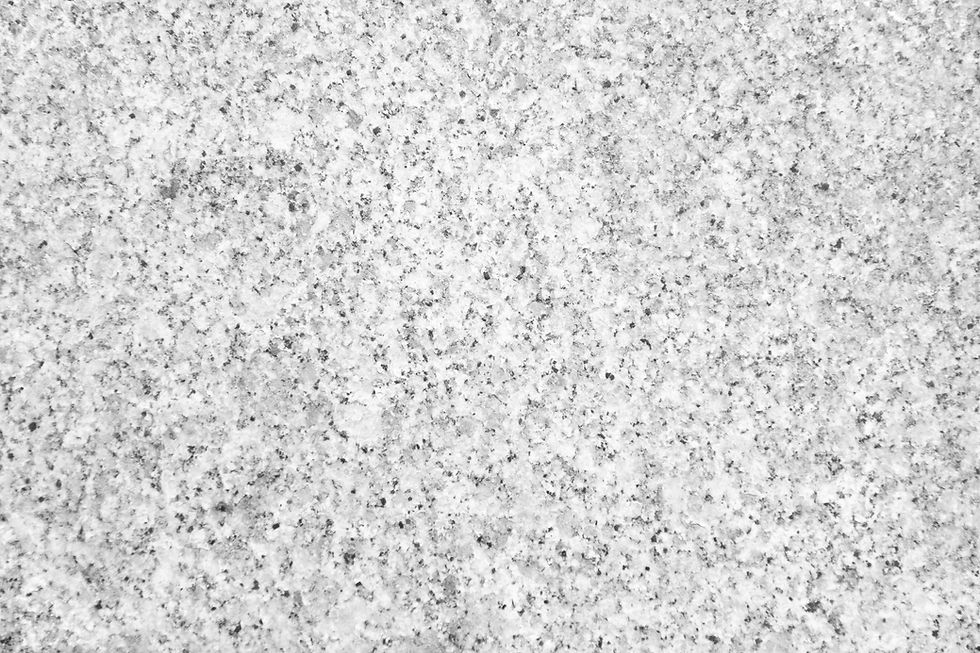 Close-up of a gray speckled granite surface with a rough texture, showing small black and white spots evenly distributed.