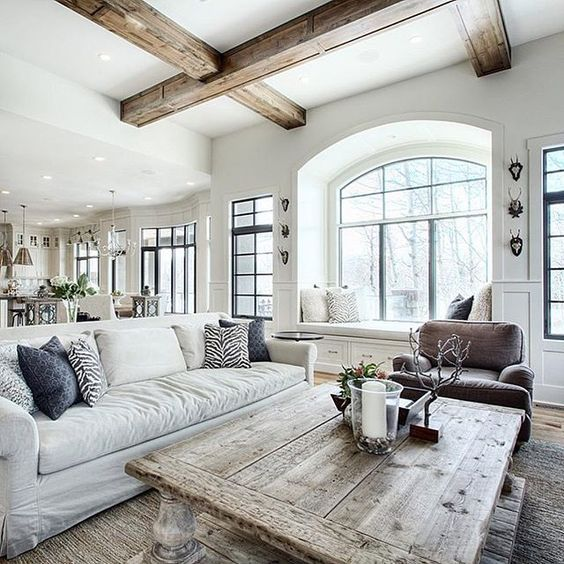 Bright living room with a large white sofa, rustic wooden table, and arched window. Cozy ambiance with neutral tones and natural light.